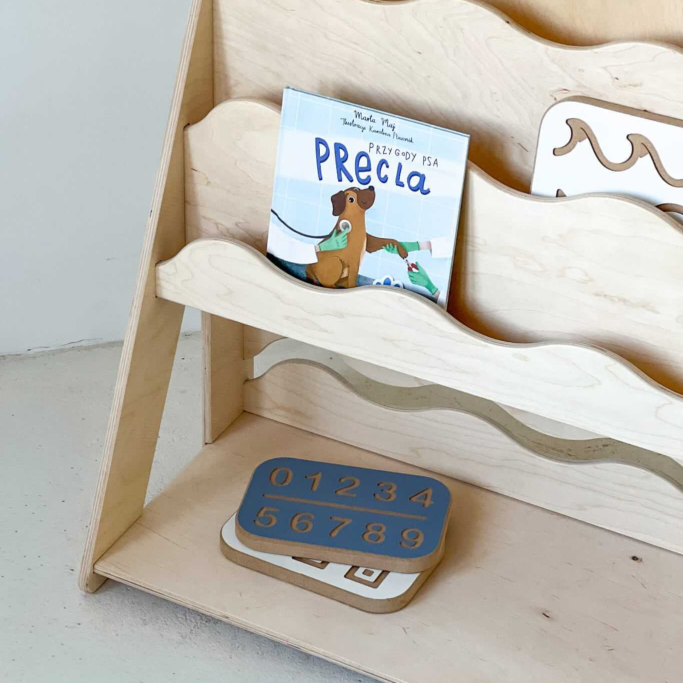 Bücher- und Spielzeugregal "WAVE" aus Holz, versch. Größen mit einem Buch und Zahlenpuzzle.