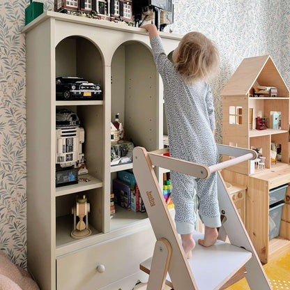 Ein Kind steht auf einem extradünnen, faltbaren Küchenhefer, um ein Modellhaus zu erreichen.