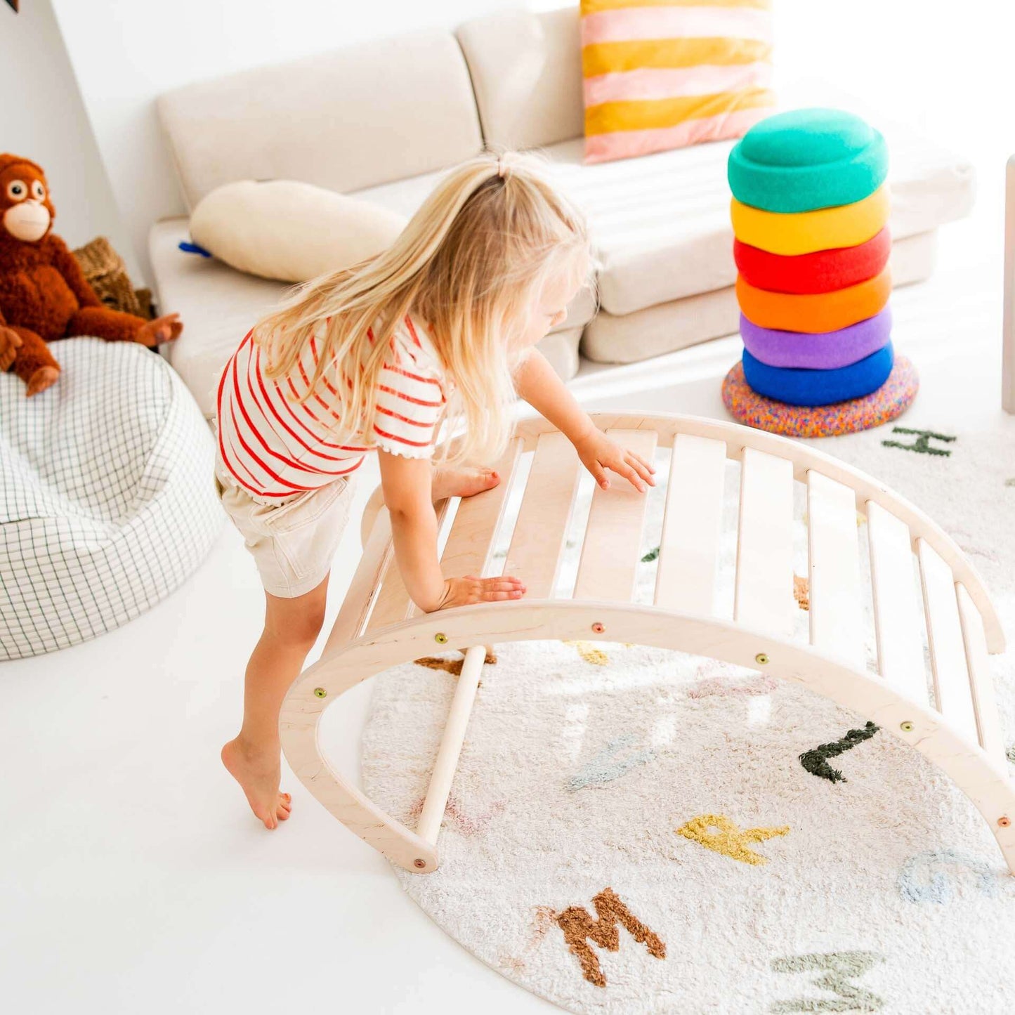 Mädchen klettert spielerisch auf Kletterbogen Äffchen in buntem Kinderspielzimmer.