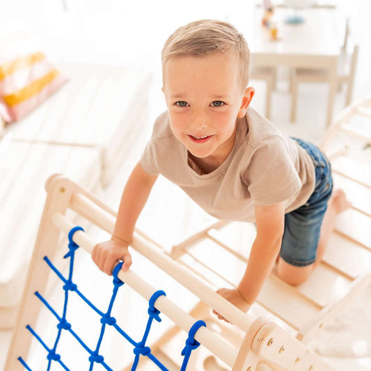 Boy climbing on the Kletterset Löwe's climbing triangle with blue rope, enjoying playtime indoors.