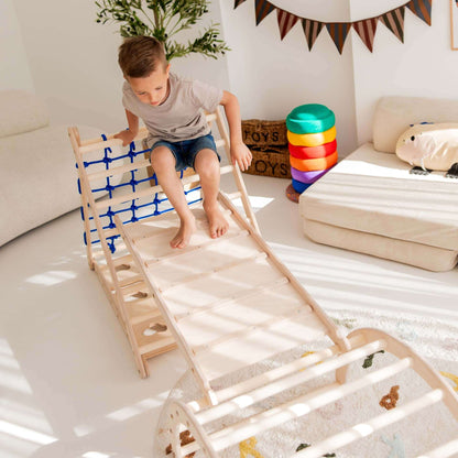 Kind mit Kletterset Löwe, das Kletterdreieck und Kletterbogen in einem hellen Spielzimmer nutzt.